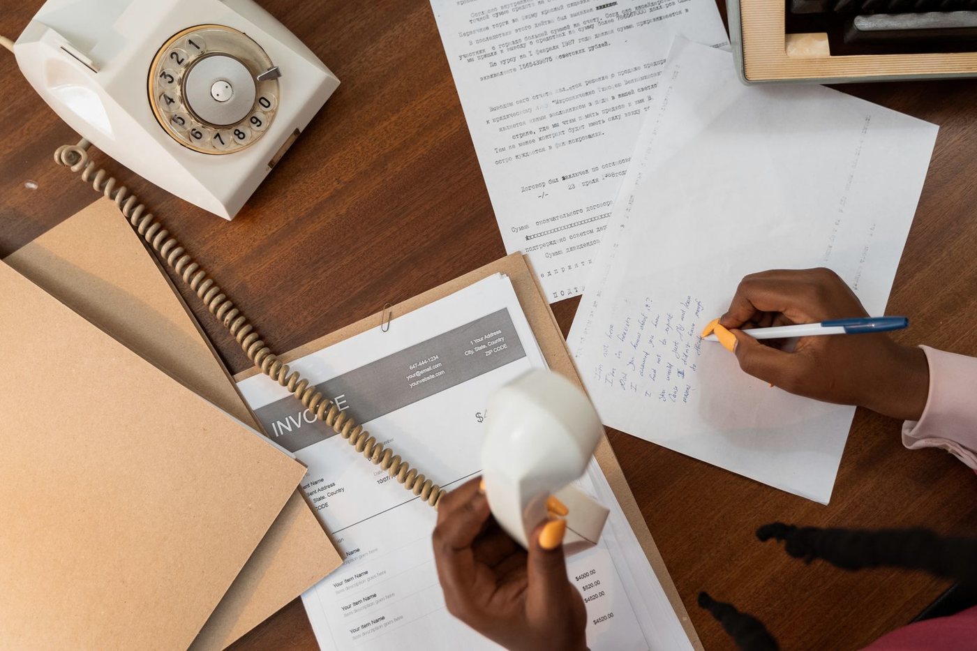Overhead view of somebody writing a note on paper while holding a telephone handset